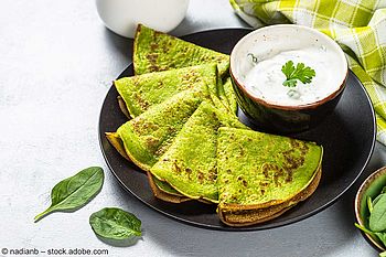 Durch Spinat grüngefärbte Pancakes mit Joghurt-Kräuter-Dip auf einem Teller
