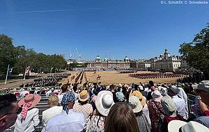 Blick von der Zuschauertribüne auf den Platz Horse Guard's Parade, wo gerade von links die Blues and Royals hineinreiten, rechts stehen die Musikkapellen