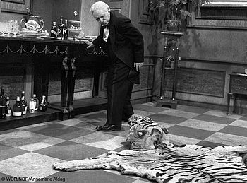 Freddie Frinton spielt im Sketch "DER 90. GEBURTSTAG ODER DINNER FOR ONE" den Diener James und stolpert wiederholt über ein Tigerfell, das auf dem Boden liegt.