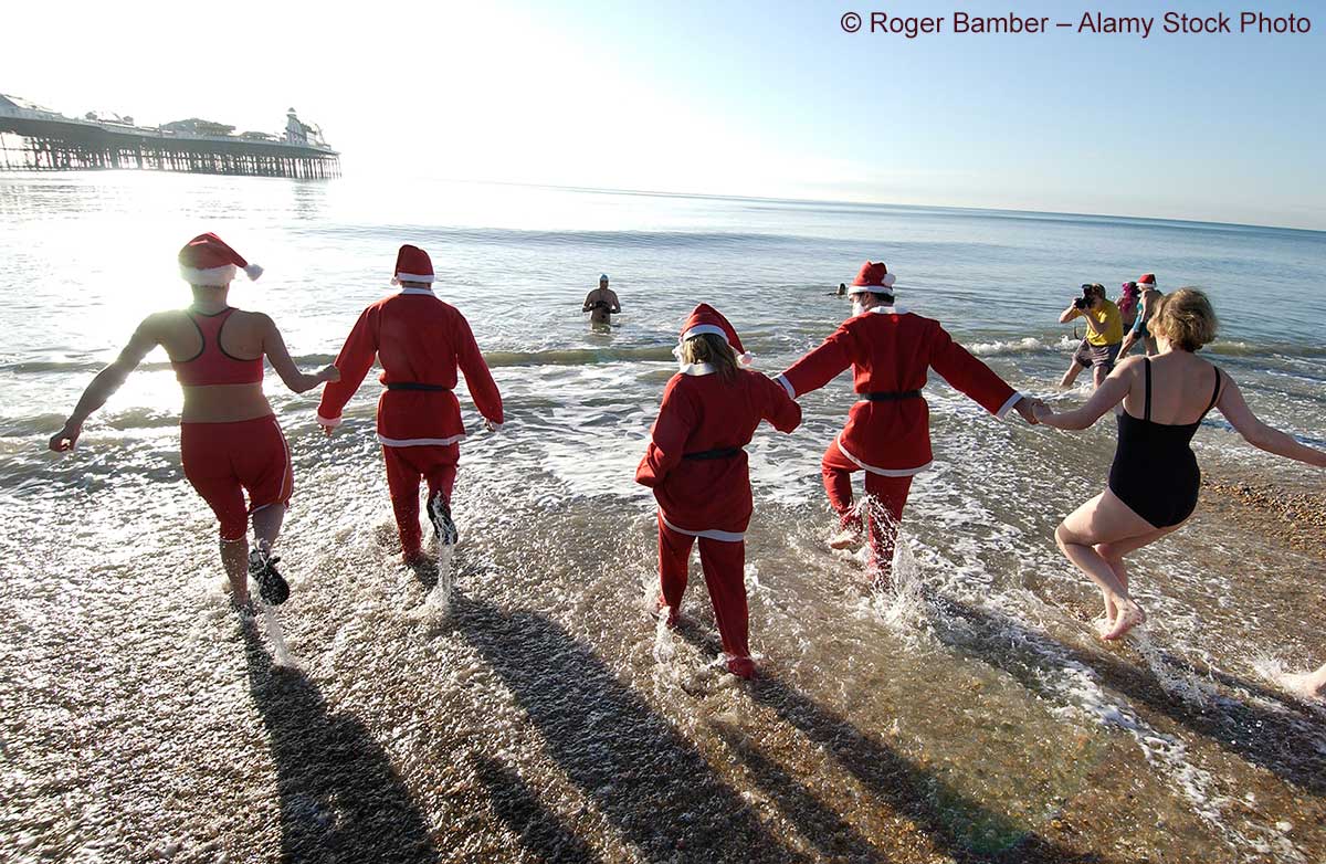 Winterschwimmer in Weihnachtsmann-Kostümen rennen ins Meer am Strand von Brighton, im Hintergrund ist das Brighton Pier zu sehen