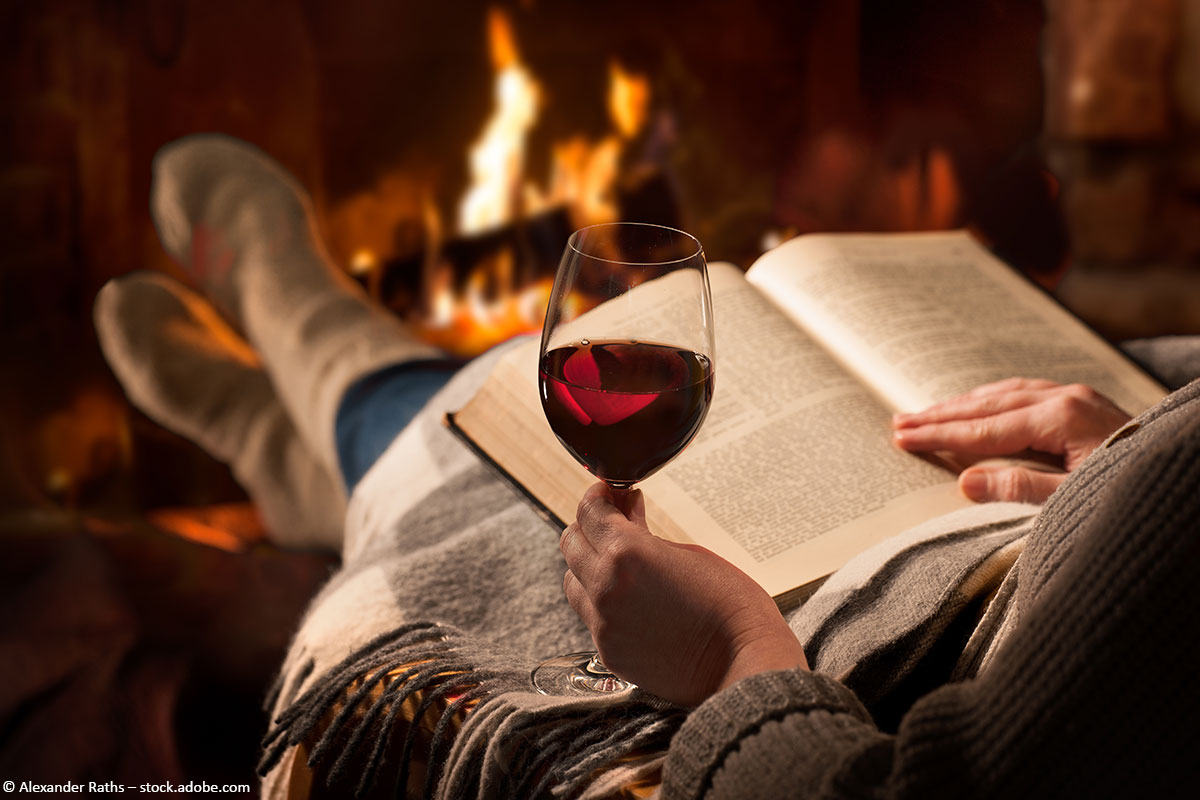 Eine Frau sitzt am Kamin mit einem Glas Rotwein und liest ein Buch